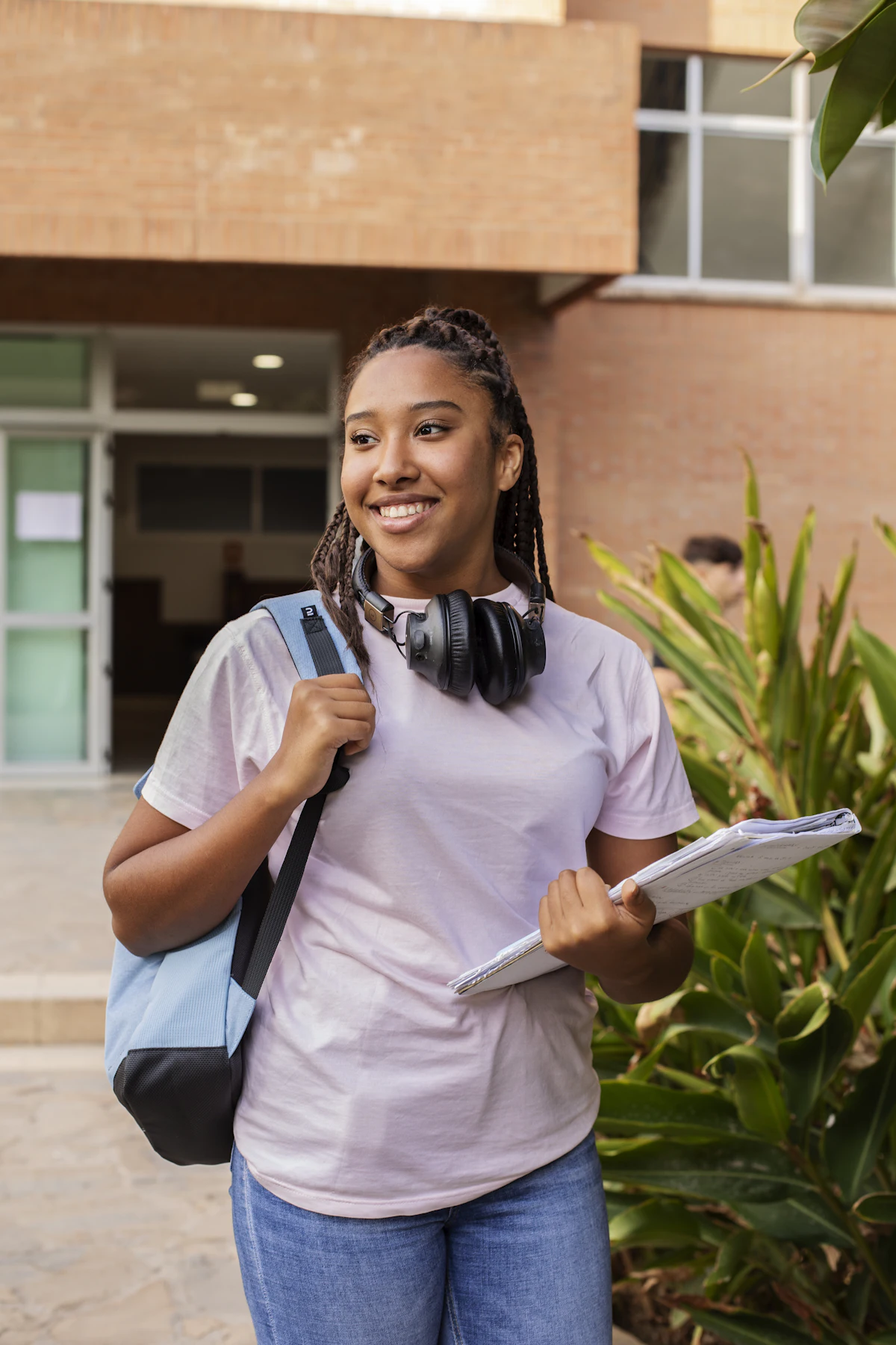 Smiling student with a backpack and notes outside her school